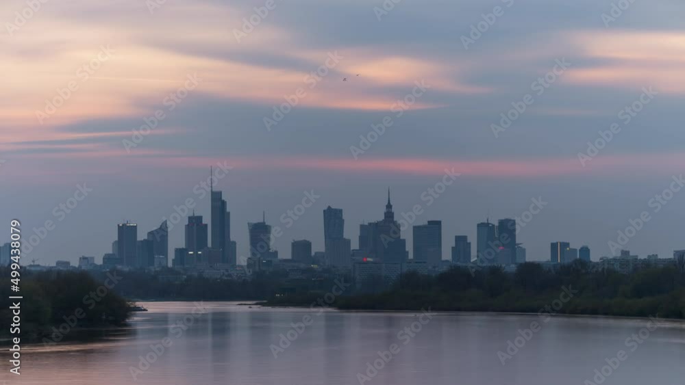 Time-lapse evening to night transition in big city of Warsaw skyline, high skyscrapers illumination reflected on Wisla river surface. Downtown beautiful cityscape panorama lit with warm sunset light Time-lapse evening to night transition in big city of Warsaw skyline, high skyscrapers illumination reflected on Wisla river surface. Downtown beautiful cityscape panorama lit with warm sunset light