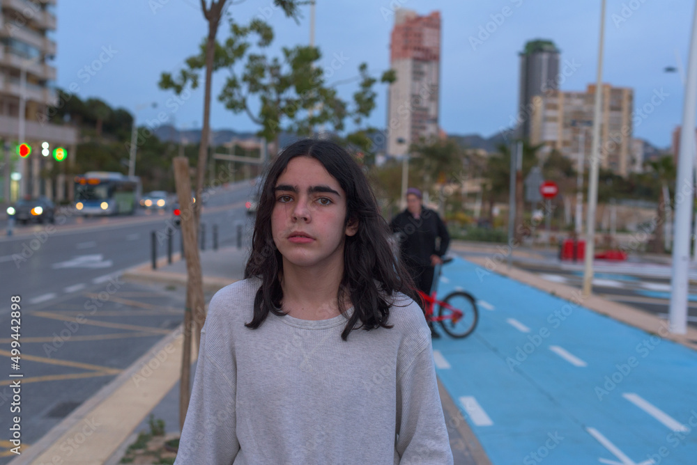 Fototapeta premium Medium close-up portrait of a transgender teenager walking along a city sidewalk at dusk.