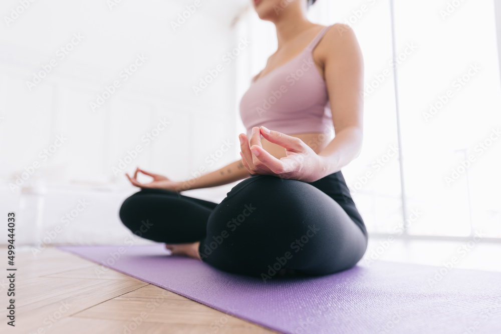 Close up meditation hand of sporty Asian woman practicing yoga on yoga mat, doing Ardha Padmasana exercise, meditating in Half Lotus pose, indoor working out at home, wearing sportswear.