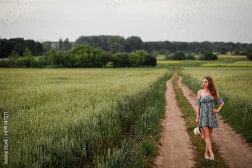 Ukrainian young girl standing in a field with green wheat, holding a hat. Beautiful nature in summer