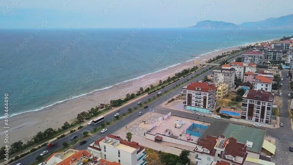 The view from the drone . Clip. The expanse of the sea with the beach, next to the road with cars and also a small piece of the city with large houses.