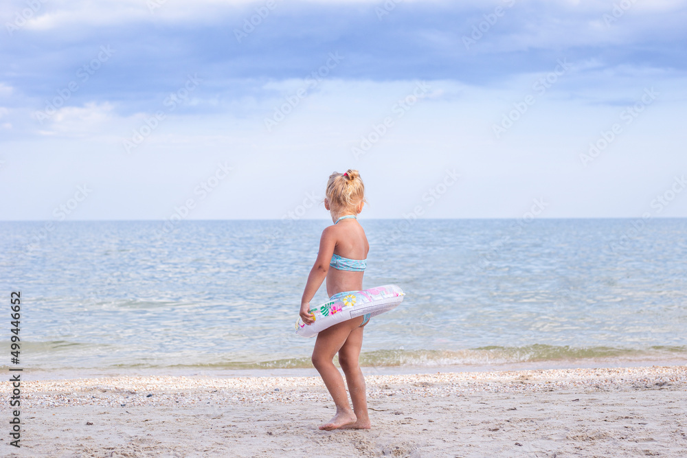 Child blond girl with a rubber ring stands on the beach. Child blond girl with a rubber ring stands on the beach.