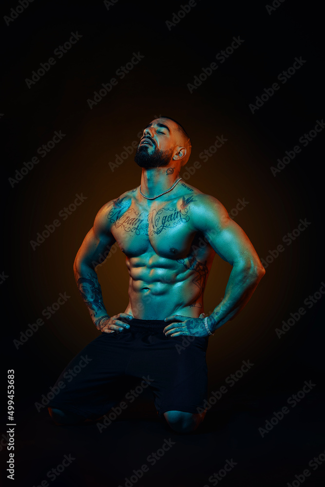 Strong and muscular man posing in the studio with colored lights Strong and muscular man posing in the studio with colored lights