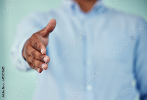 Welcome. Cropped shot of an unrecognizable businessman standing with his hand outstretched for a handshake against a blue background.