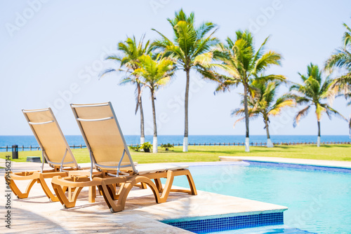 Poolside lounge beds on the beach with a view of the ocean and palm trees