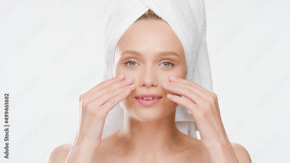 Close-up beauty portrait of cute European young slim woman with towel on her head touches her cheeks after bathing on white background | Acne prevention concept Close-up beauty portrait of cute European young slim woman with towel on her head touches her cheeks after bathing on white background | Acne prevention concept