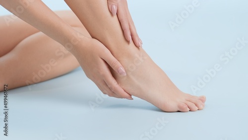 Close-up shot of woman touches her foot and heel sitting on the floor on pale blue background   Leg care commercial concept