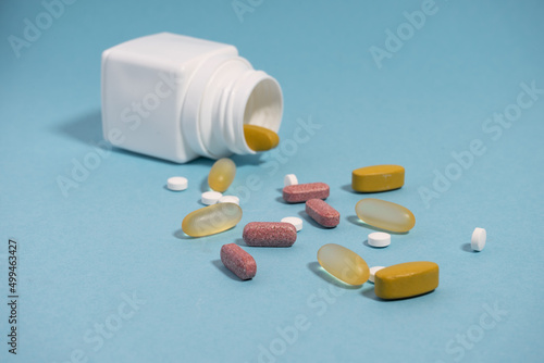 The colored pills and vitamins and white container on the blue background