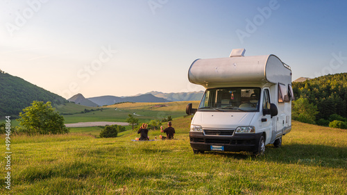 Obraz na płótnie Couple having beer near camper van in Montelago highlands, Marche, Italy. Romantic sunset, unique hills and mountains landscape, alternative vanlife vacation concept. w salonie