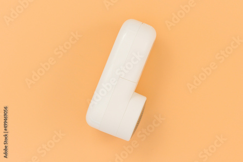 Side view of a portable white lint remover on an orange background. Clothes. Fabric. Clean. Remover. Textile. Removal. Clothing. Remove. White. Lint. Electric. Object.