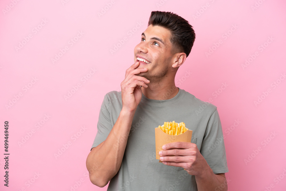 Young caucasian man holding fried chips isolated on pink background looking up while smiling Young caucasian man holding fried chips isolated on pink background looking up while smiling
