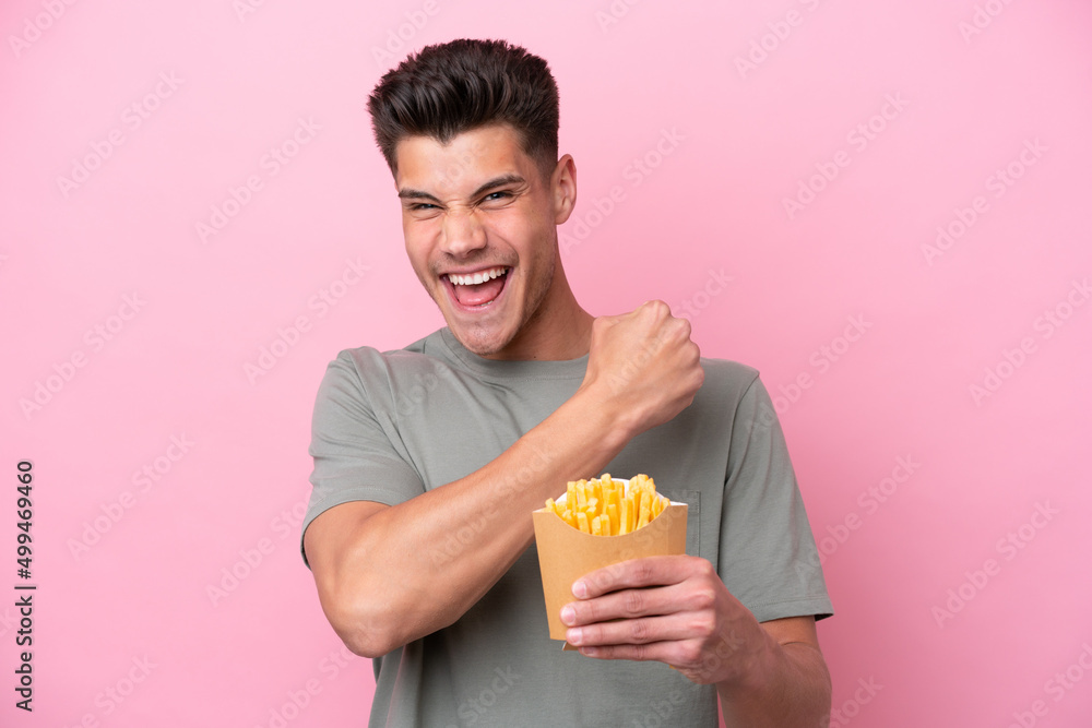 Young caucasian man holding fried chips isolated on pink background celebrating a victory Young caucasian man holding fried chips isolated on pink background celebrating a victory