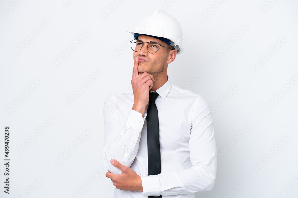 Young architect caucasian man with helmet and holding blueprints isolated on white background having doubts while looking up Young architect caucasian man with helmet and holding blueprints isolated on white background having doubts while looking up