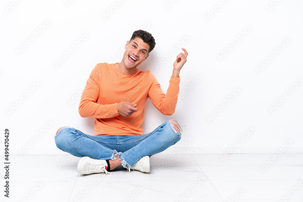 Young man sitting on the floor isolated on white background making guitar gesture Young man sitting on the floor isolated on white background making guitar gesture