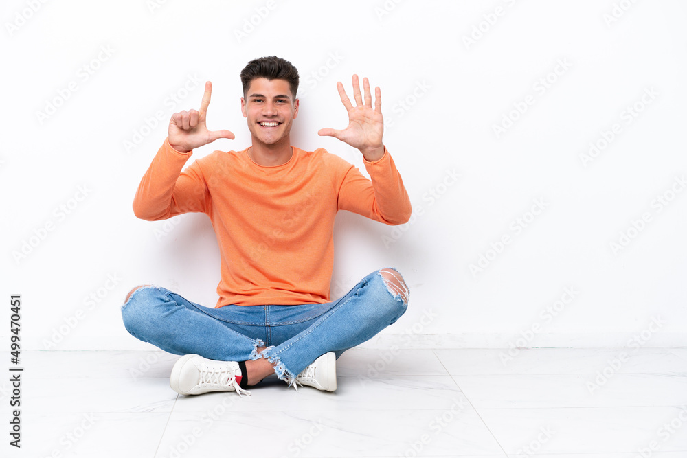 Young man sitting on the floor isolated on white background counting seven with fingers Young man sitting on the floor isolated on white background counting seven with fingers
