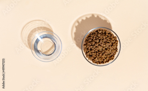 Top view of white bowl with dry kibble cat food and wateer on beige background.  photo