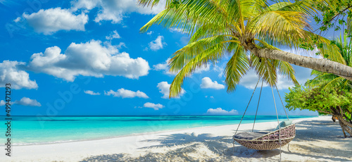 Tropical beach panorama as summer relax landscape with beach swing or hammock hang on palm tree over white sand sea beach banner. Amazing beach vacation summer holiday concept. Luxury romantic travel