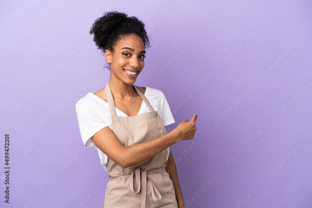 Restaurant waiter latin woman isolated on purple background pointing back