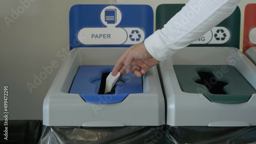 Throwing a piece of paper in a special bin for waste recycling, concept of ecology. HDR. Close up of male hand putting a small sheet of paper in a recycling bin. photo