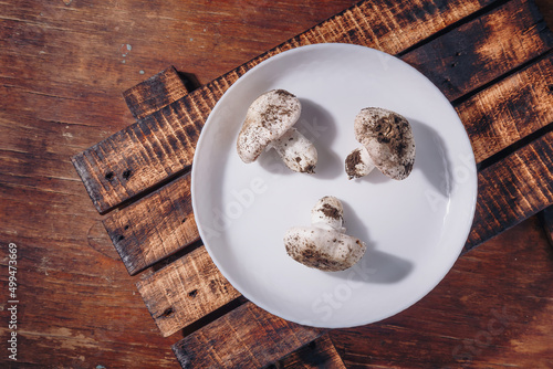 Fresh raw unwashed champignons on plate  wooden kitchen table. Dirty unprepared ingredient  cooking tasty meal  healthy eating. Top view closeup