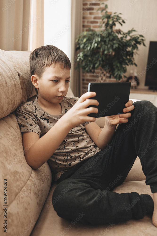 Teenage boy sitting on couch using tablet and playing video games on internet online at cozy home. Teenage boy sitting on couch using tablet and playing video games on internet online at cozy home.