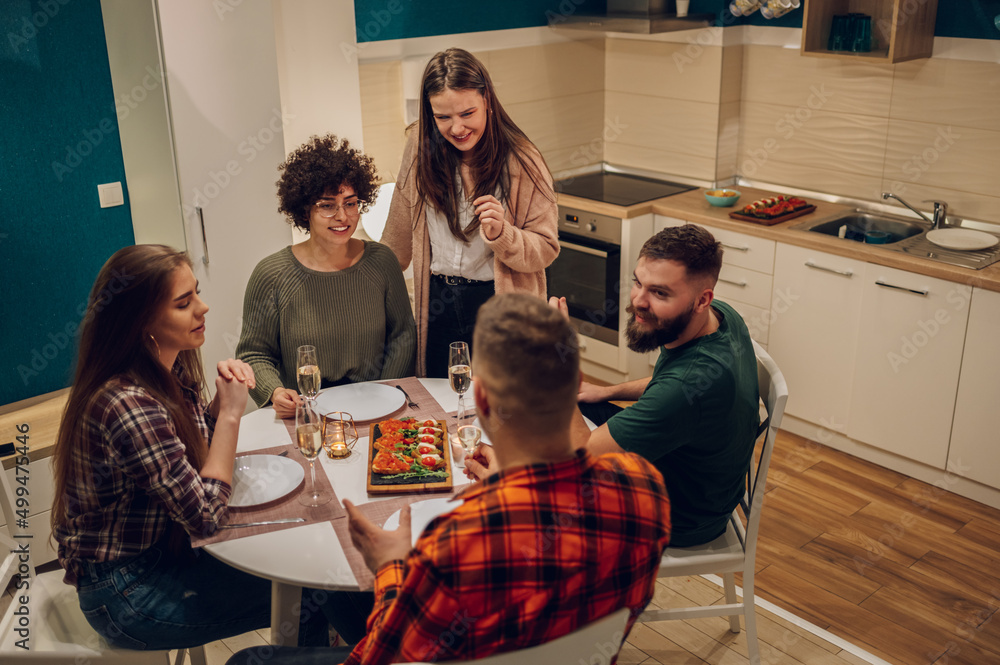 Fototapeta premium Group of friends enjoying dinner while sitting at the kitchen table together