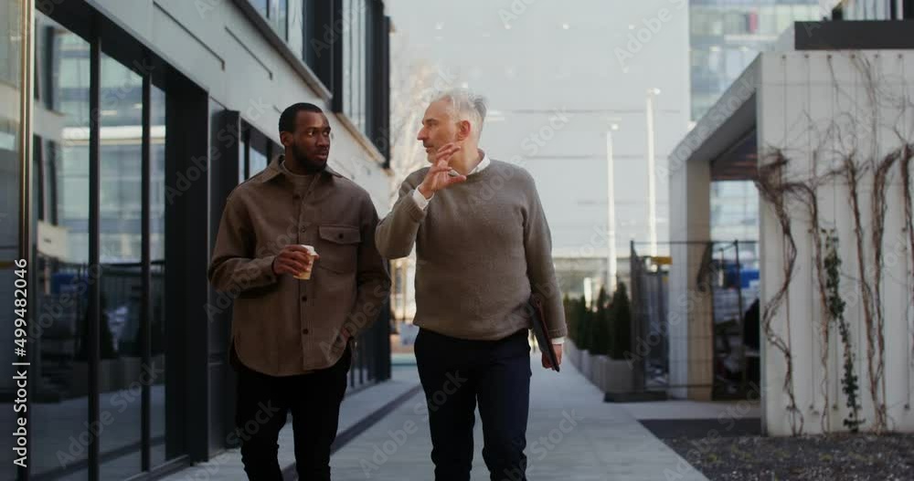 Two men of different ages and nationalities are talking walking in office center Two men of different ages and nationalities are talking walking in office center