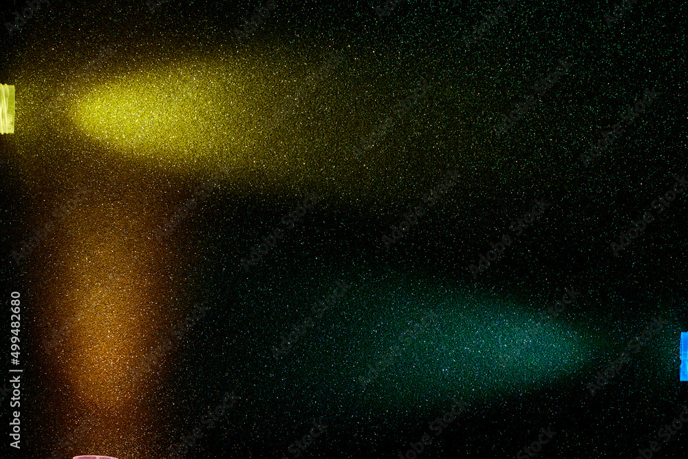 On a dark green background in fine grain, rays of yellow dark turquoise and orange light On a dark green background in fine grain, rays of yellow dark turquoise and orange light