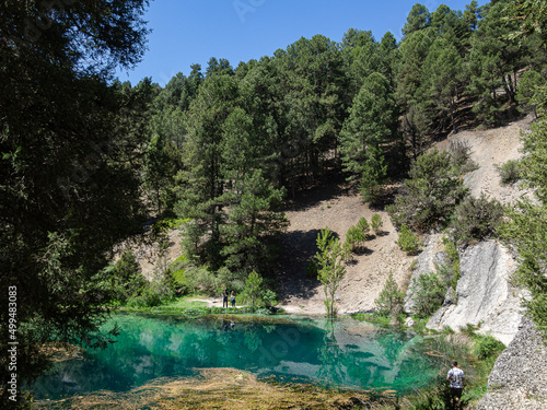 La Fuentona de Muriel en Soria, España, verano de 2021. Lago con aguas turquesas rodeado de árboles verdes y turistas disfrutando.