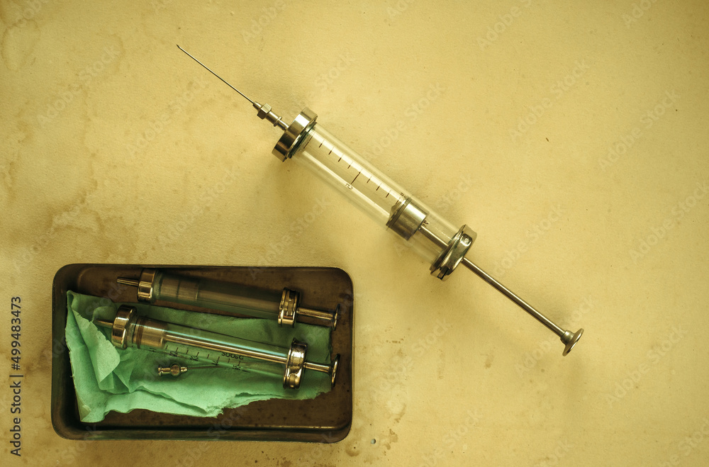 An old glass syringe with a needle on a yellowed sheet of paper
