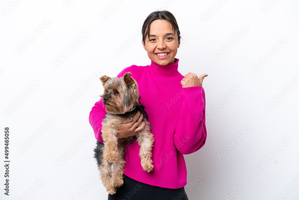 Young hispanic woman holding a dog isolated on white background pointing to the side to present a product Young hispanic woman holding a dog isolated on white background pointing to the side to present a product