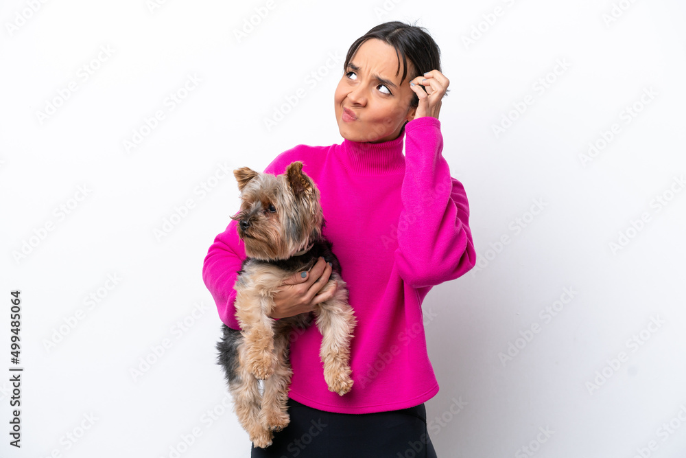 Young hispanic woman holding a dog isolated on white background having doubts and with confuse face expression Young hispanic woman holding a dog isolated on white background having doubts and with confuse face expression