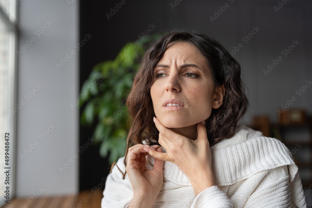 © DimaBerlin - Young sick worried woman with sore throat at home touching neck, unhealthy female wrapped in plaid having swollen lymph nodes caused by bacterial infection, feeling pain or discomfort while swallowing