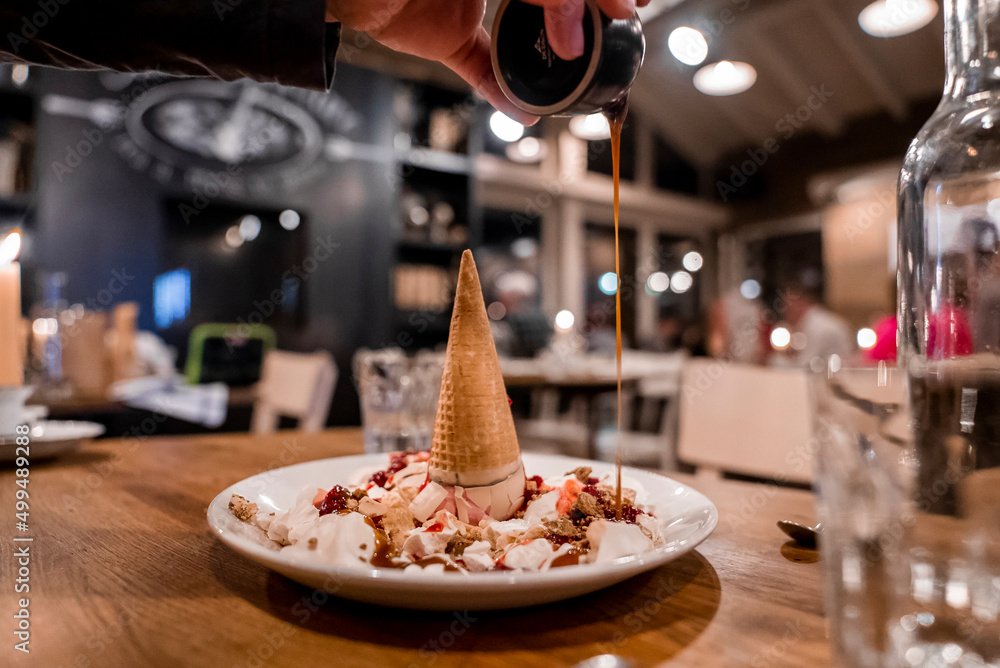 Fototapeta premium Man pouring caramel over delicious ice cream dessert on table at restaurant