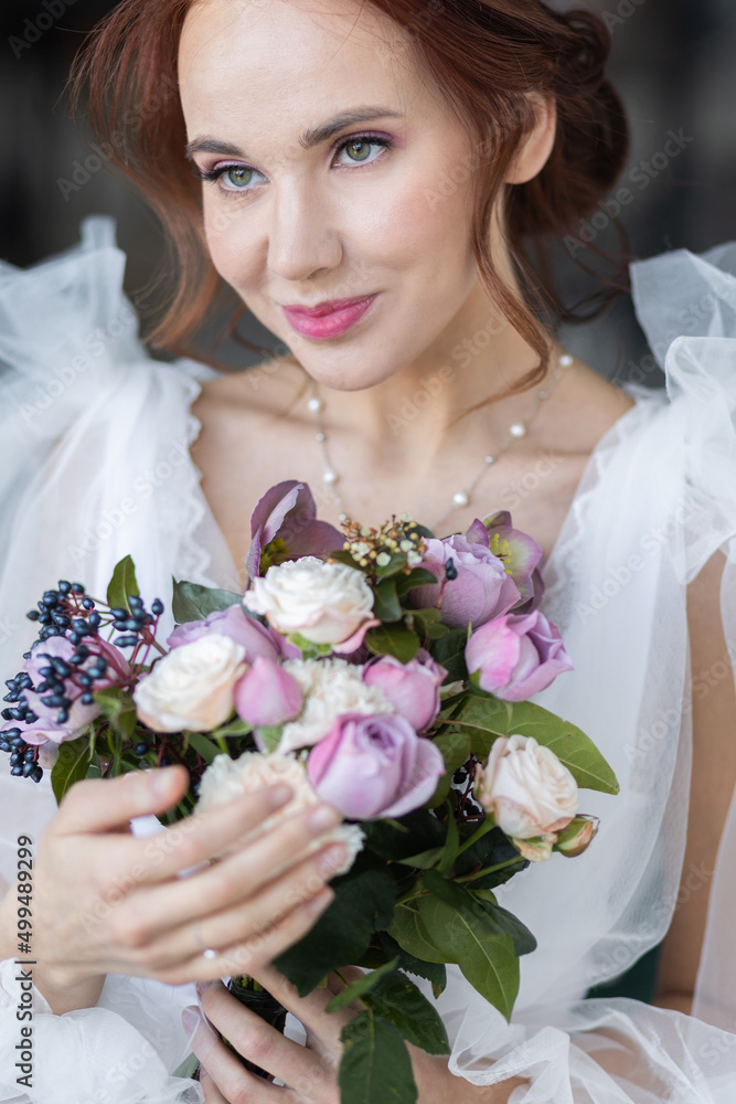 Naklejka premium Beautiful attractive caucasian young woman in a white wedding dress with a bridal flower bouquet. Smiling