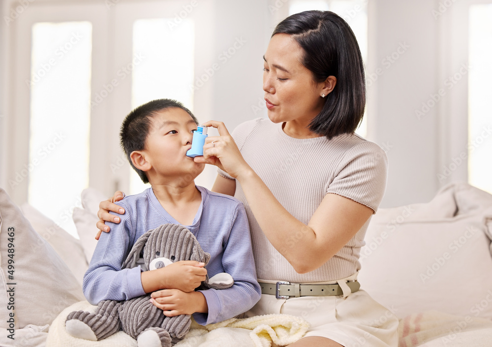 Breathe in slowly. Shot of a woman helping her son with his asthma inhaler.