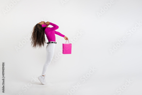 Young woman standing on tiptoe talking on phone and holding shopping bag on white background photo