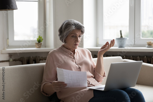Foto Older woman sit on sofa put wireless computer on laps, check bills, experiences problems with payments looks concerned