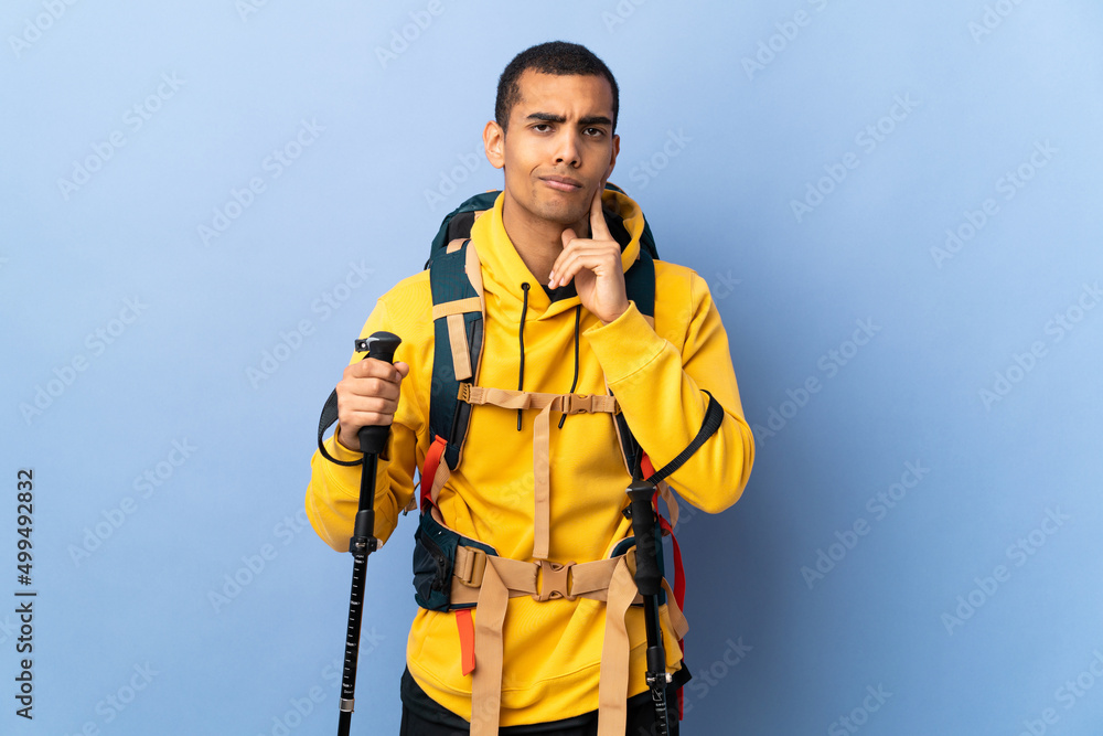 African American man with backpack and trekking poles over isolated background and thinking African American man with backpack and trekking poles over isolated background and thinking