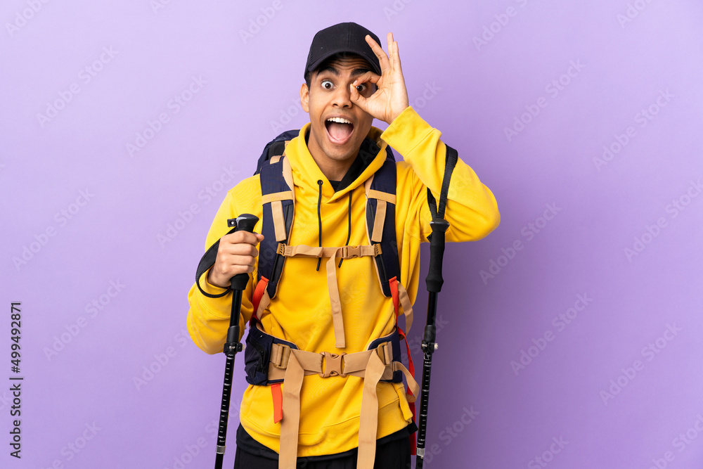 African American man with backpack and trekking poles over isolated background showing ok sign with fingers African American man with backpack and trekking poles over isolated background showing ok sign with fingers