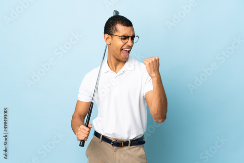 African American man over isolated blue background playing golf and celebrating a victory