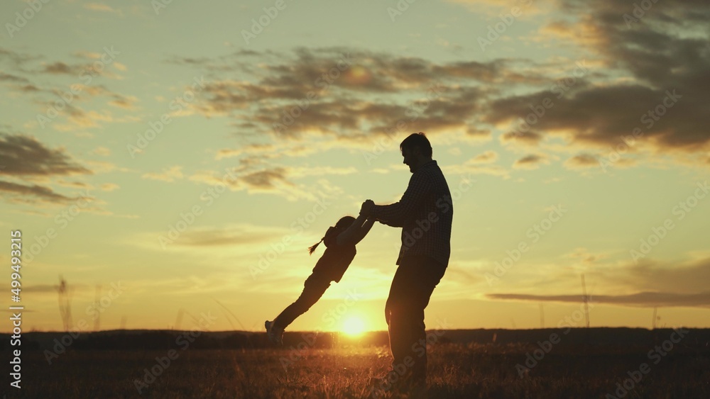 Father circles hands of his beloved baby in sun on field, baby laughs in flight. Dad, child, daughter are playing in park at sunset. Healthy family and childhood. Happy family. Child have fun in