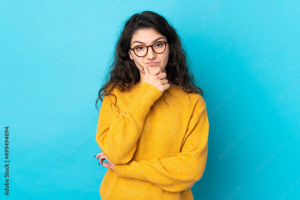 Fototapeta premium Teenager Russian girl isolated on blue background thinking