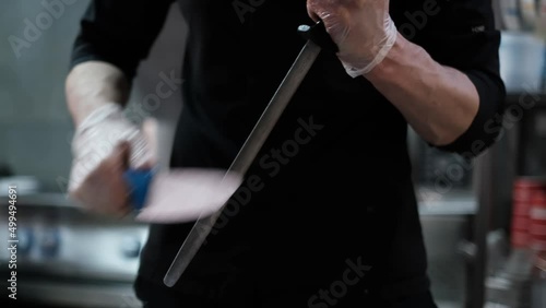 Close-up of sushi chef in gloves slices fresh salmon at sushi bar. Professional cook cutting fish fillet at commercial kitchen, slow motion.