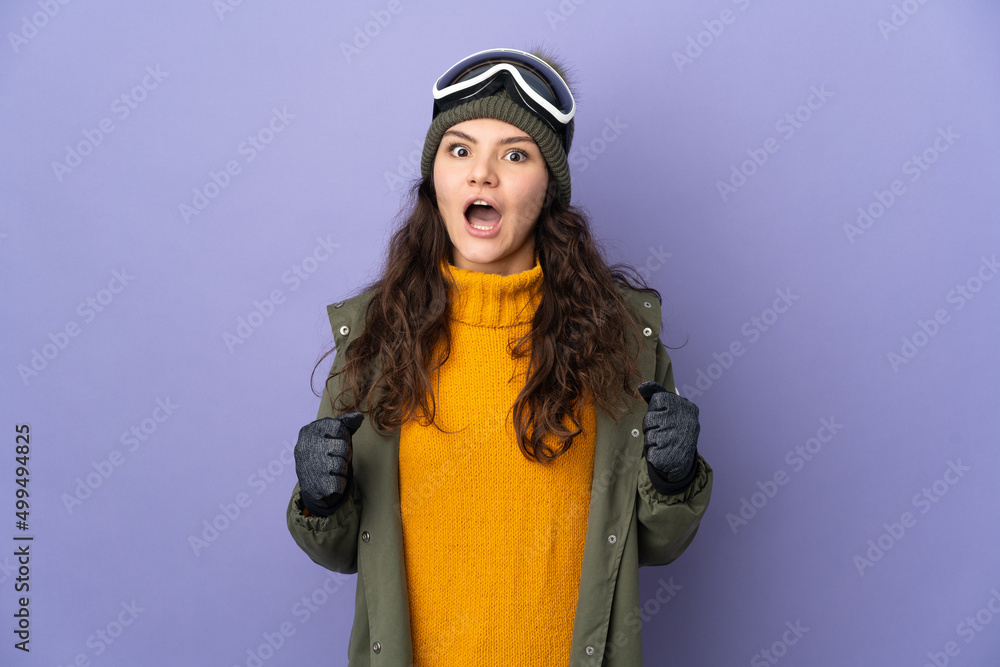 Teenager Russian girl with snowboarding glasses isolated on purple background celebrating a victory in winner position Teenager Russian girl with snowboarding glasses isolated on purple background celebrating a victory in winner position