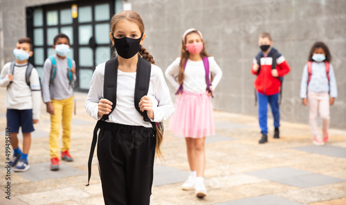Portrait of tween schoolgirl in protective face mask with rucksack on her way to college on warm fall day. Back to school after lockdown concept.