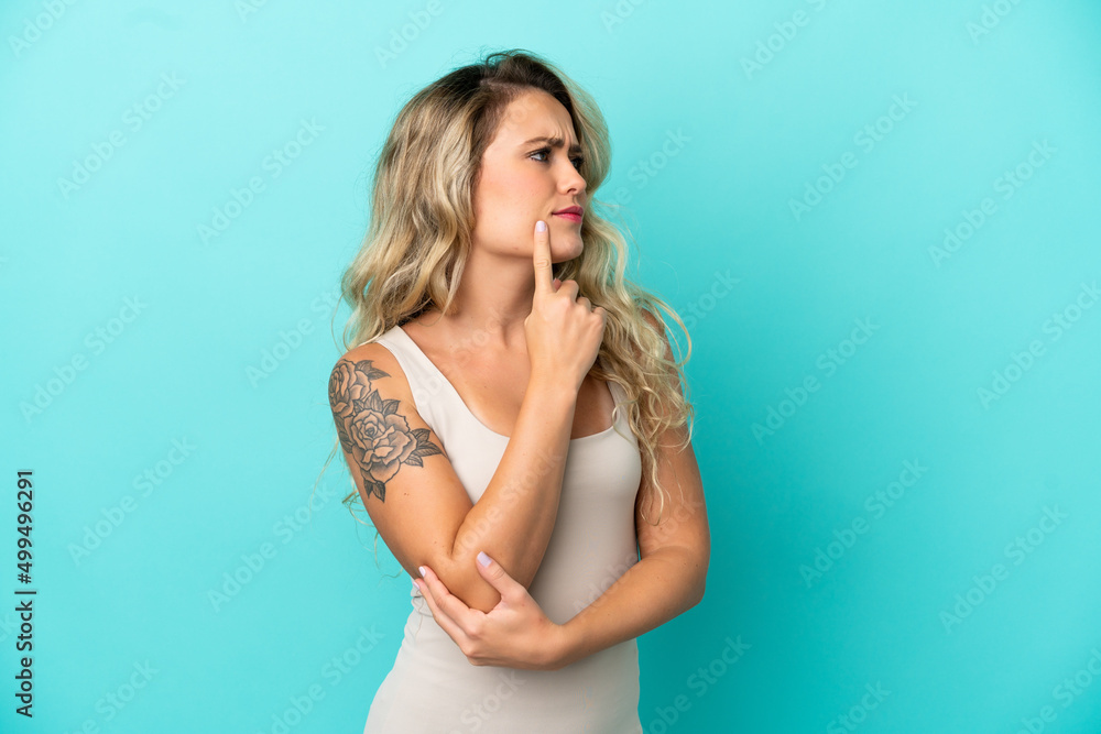 Young Brazilian woman isolated on blue background having doubts while looking up Young Brazilian woman isolated on blue background having doubts while looking up