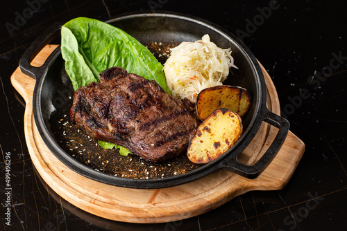 Grilled steak with baked golden potatoes served with sour cabbage and red sauce on a dark background. Delicious Recipe. Pork Fillet Cooked on Skillet for Dinner . Fried Juicy Meat Texture.