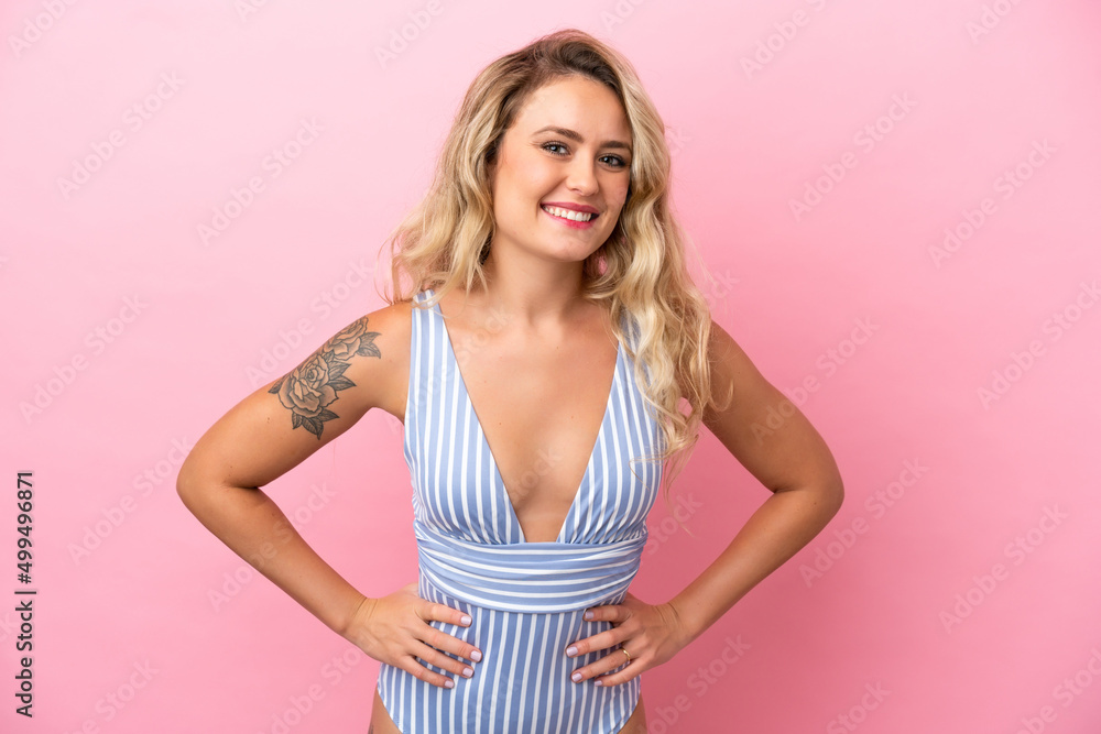 Young Brazilian woman in swimsuit in summer holidays isolated on pink background posing with arms at hip and smiling Young Brazilian woman in swimsuit in summer holidays isolated on pink background posing with arms at hip and smiling