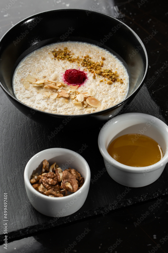 Semolina porridge for breakfast oat with nuts in black bowl served with honey isolated on black stone background. Homemade food. Tasty breakfast. Selective focus. Semolina porridge for breakfast oat with nuts in black bowl served with honey isolated on black stone background. Homemade food. Tasty breakfast. Selective focus.
